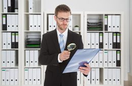 Young businessman looking at document through magnifying glass in office