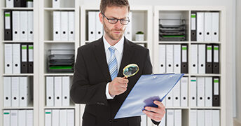 Young businessman looking at document through magnifying glass in office